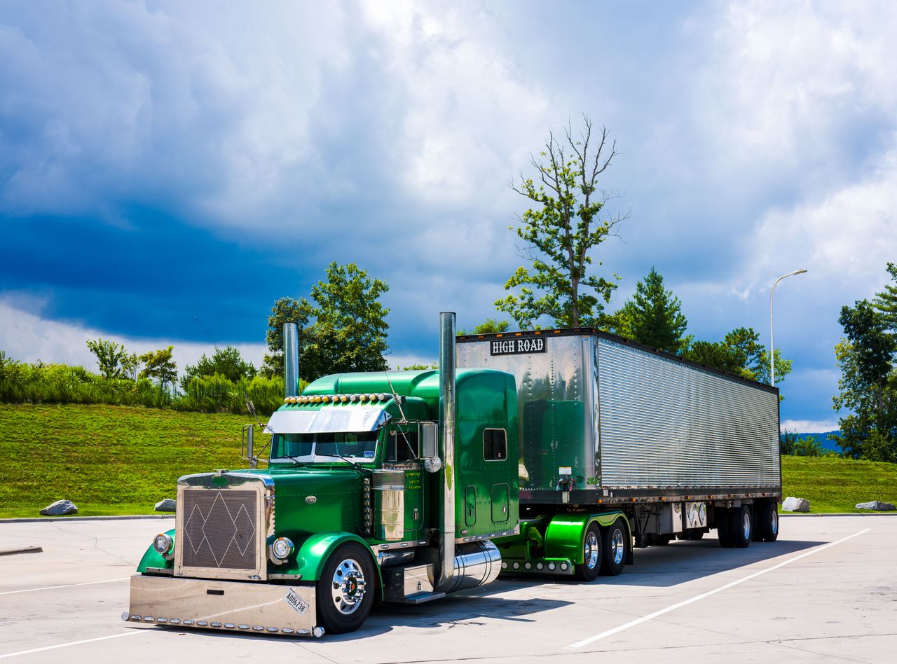 A striking green semi-truck parked outdoors with a dramatic cloudy sky backdrop.